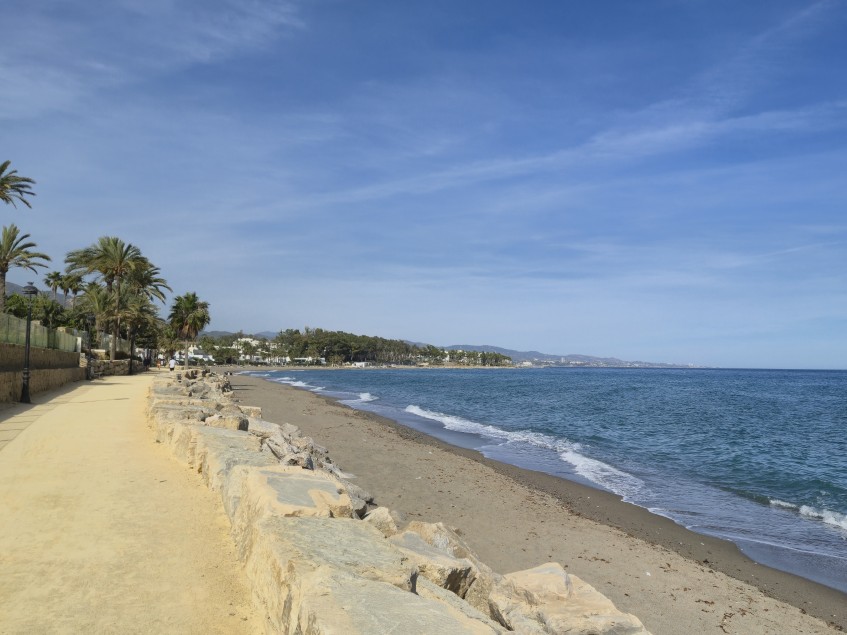 View along the Paseo Marítimo in Marbella showing the Mediterranean coastline, palm trees and walkway on a calm afternoon on the Costa del Sol.