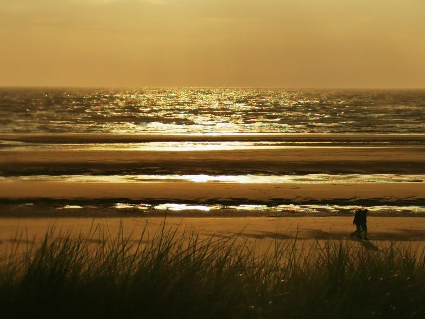 Herbstsonnenuntergang am Strand von Marbella mit einem spazierenden Paar Weiches Herbstlicht an der Costa del Sol, Strand von Marbella bei Sonnenuntergang mit einem Paar, das am Meer spaziert